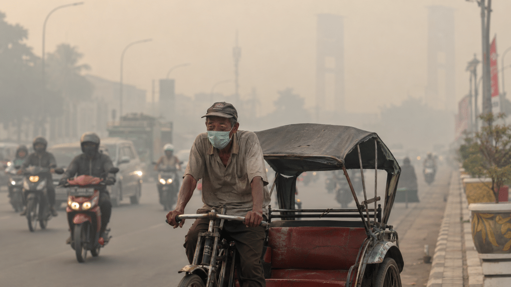 Warga Palembang Merana, Asap Karhutla Pekat Paksa Siswa Dipulangkan 3 Penarik becak mengenakan masker berjuang mengayuh becaknya menembus kabut asap tebal dengan latar belakang Jembatan Ampera yang samar.